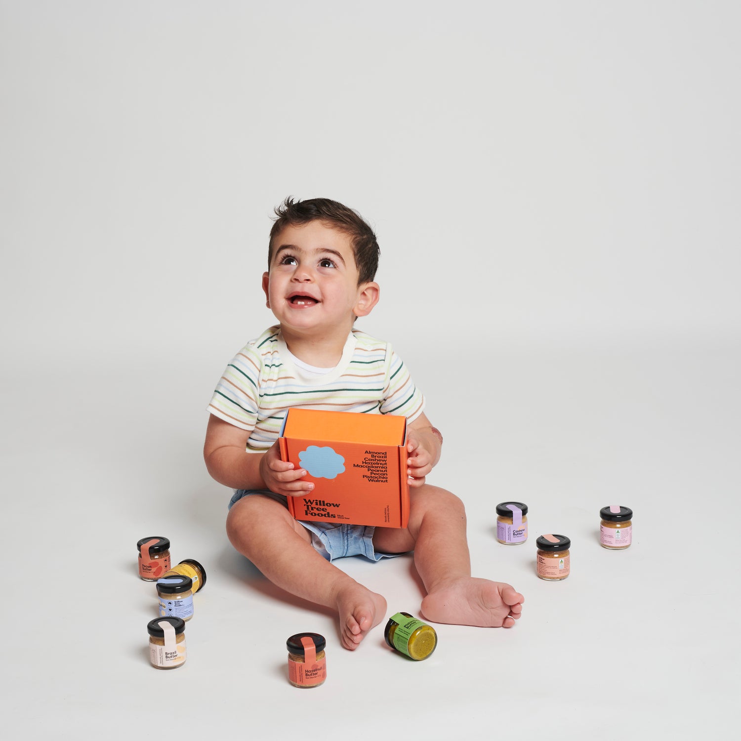 Baby smiling while holding a box of Willow Tree Foods Nut Butter Jars